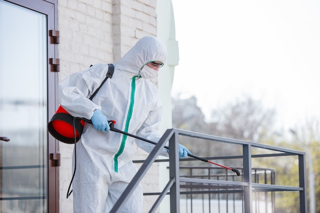 Pandemia di coronavirus. Un disinfettante in tuta protettiva e maschera spruzza disinfettanti nella stanza.