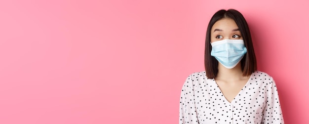 Pandemia di Covid e concetto di stile di vita bellissima modella asiatica femminile in maschera medica che guarda a sinistra al co