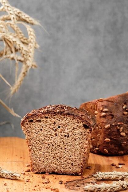 Pane a lievitazione naturale di grano e segale appena sfornato con semi di girasole su un tagliere. Metà del pane su un fuoco selettivo del primo piano della tavola di legno. Spighe di grano sul tavolo