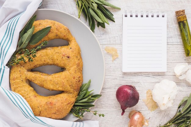 Pane appena sfornato con ingredienti e blocco note sul contesto in legno