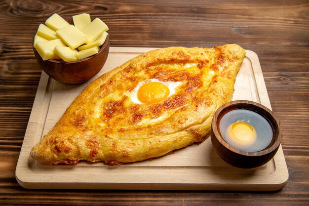 Pane appena sfornato di vista frontale con l'uovo cotto sul cibo a base di uova della colazione del panino del pasto della pasta dello scrittorio di legno marrone