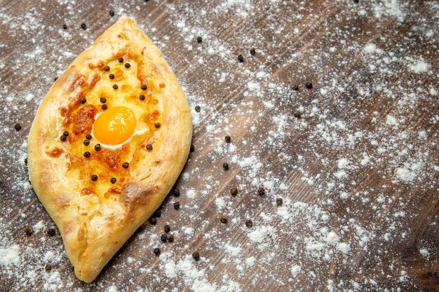 Pane appena sfornato di vista frontale con l'uovo e la farina cucinati sulla pasta marrone dello scrittorio cuocere il panino del pane dell'uovo