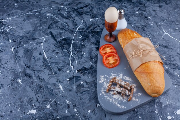 Pane baguette, verdure a fette, uovo sodo a bordo sul blu.