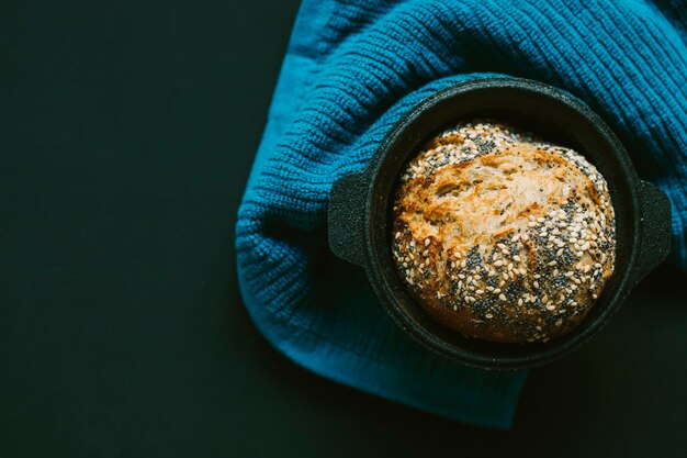 Pane casalingo con i semi nel contenitore nero sul tessuto contro fondo nero