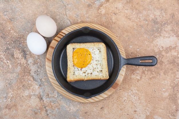 Pane con uova fritte in padella nera con uova crude