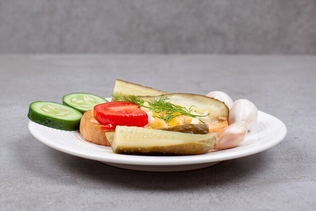 Pane con uova strapazzate e sottaceti sulla zolla bianca