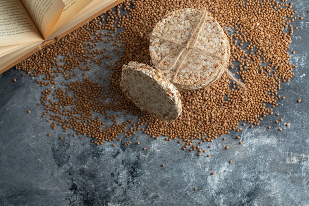 Pane croccante, grano saraceno crudo e libro sulla superficie di marmo