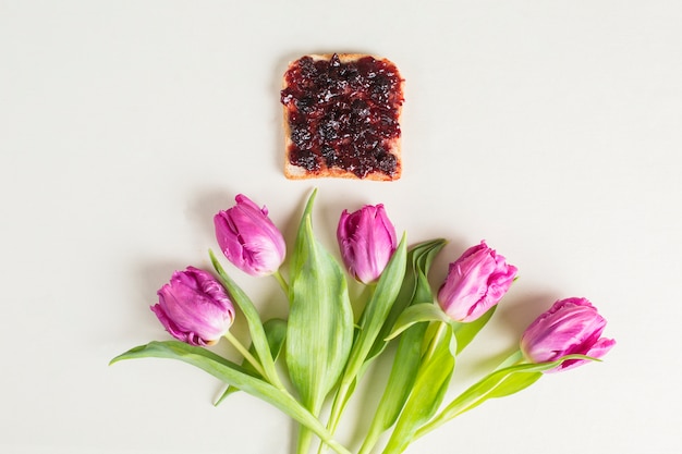 Pane e marmellata di bacche sopra i tulipani viola su sfondo bianco