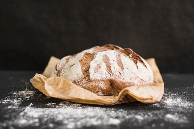 Pane rotondo della segale rustica di recente al forno rotonda su carta marrone contro fondo nero