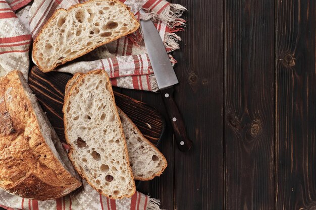 Pane rustico a fette senza impastare su un tagliere su un vecchio tavolo rustico con spazio per la copia su sfondo scuro Disposizione del pane integrale fatto in casa sul tavolo