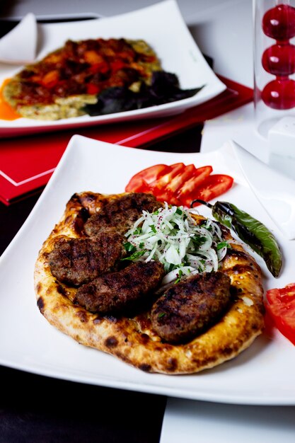 Pane Tandoor con polpette fritte servito con pepe affumicato, fette di cipolla e fette di pomodoro