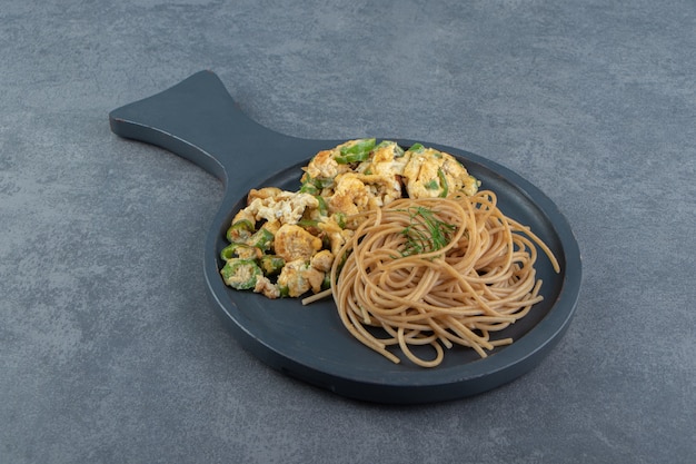 Pane tostato con insalata e spaghetti su tavola nera.