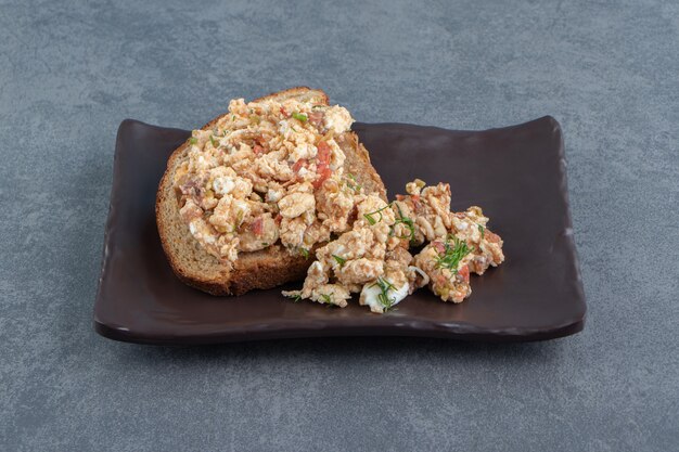 Pane tostato con insalata e uova su un piatto scuro.