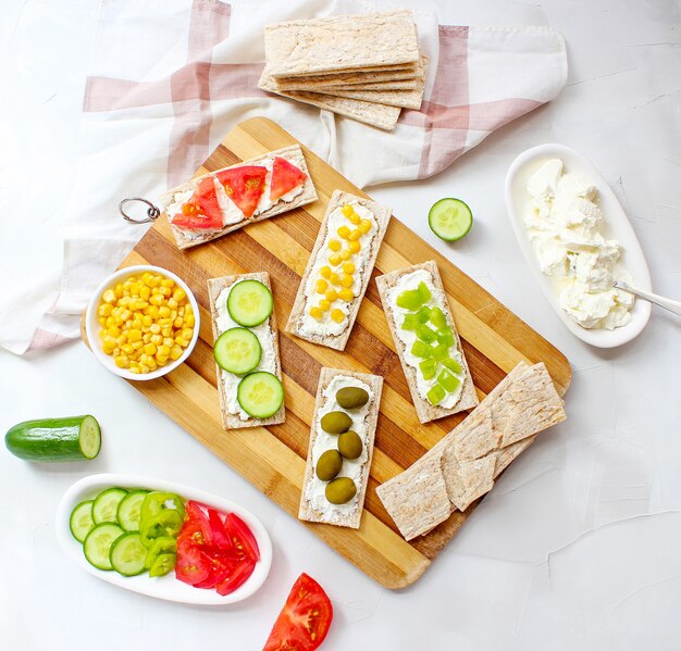 Pane tostato croccante fatto in casa con ricotta e olive verdi, fette di cavolo, pomodori, mais, peperone verde sul tagliere. Concetto di cibo sano, vista dall'alto. Flat Lay