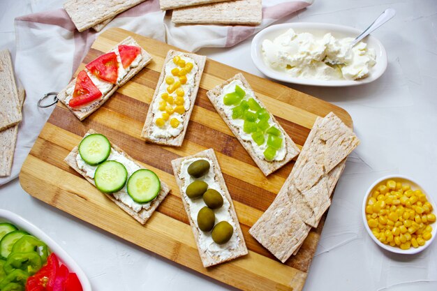 Pane tostato croccante fatto in casa con ricotta e olive verdi, fette di cavolo, pomodori, mais, peperone verde sul tagliere. Concetto di cibo sano, vista dall'alto. Flat Lay