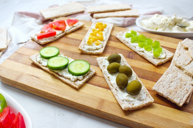 Pane tostato croccante fatto in casa con ricotta e olive verdi, fette di cavolo, pomodori, mais, peperone verde sul tagliere. Concetto di cibo sano, vista dall'alto. Flat Lay