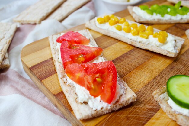 Pane tostato croccante fatto in casa con ricotta e olive verdi, fette di cavolo, pomodori, mais, peperone verde sul tagliere. Concetto di cibo sano, vista dall'alto. Flat Lay