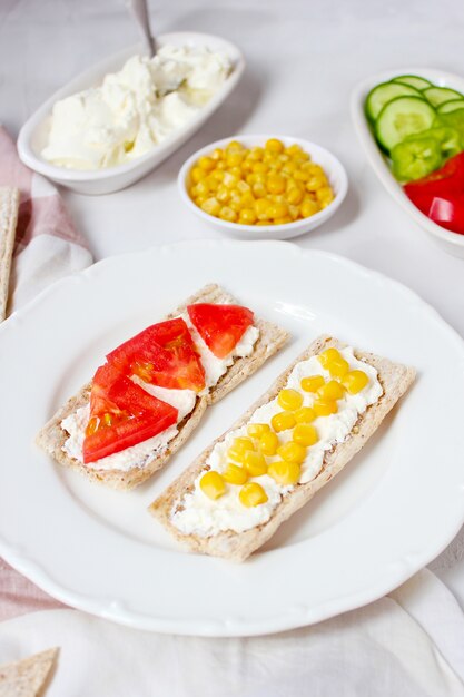 Pane tostato croccante fatto in casa con ricotta e olive verdi, fette di cavolo, pomodori, mais, peperone verde sul tagliere. Concetto di cibo sano, vista dall'alto. Flat Lay