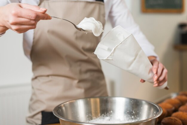 Panettiere femminile che riempie panna montata nel sacchetto di glassa bianco