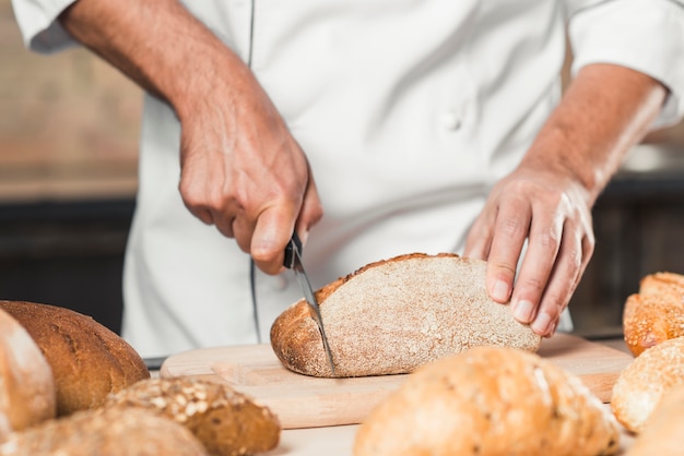 Panettiere maschio che taglia la pagnotta sul tagliere del pane