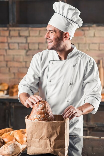 Panettiere maschio sorridente che mette pane in sacco di carta marrone