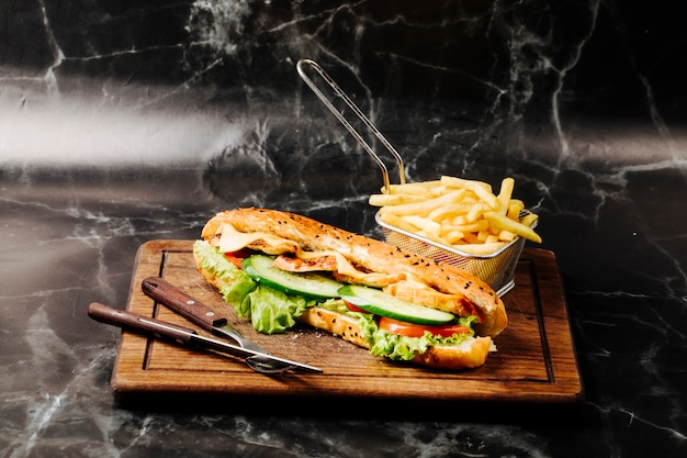 Panino baguette con ingredienti misti e patatine fritte su una tavola di legno.