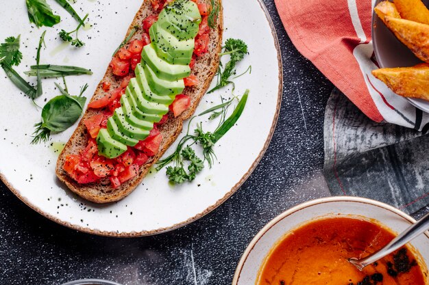 Panino con pomodoro, cetriolo ed erbe verdi con una ciotola di zuppa di lenticchie.