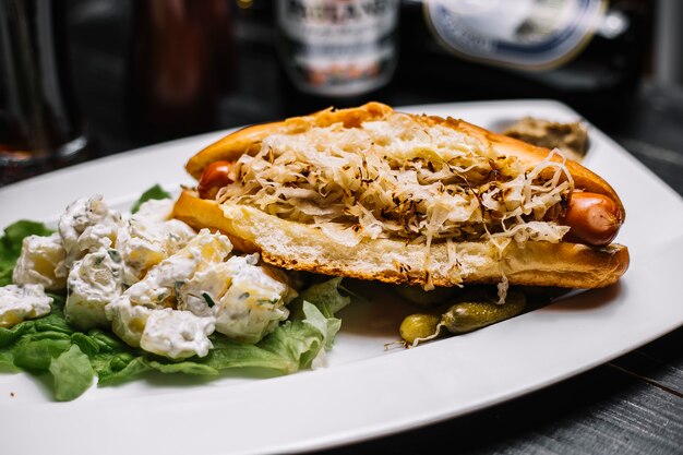 Panino con salsiccia arrostita all'interno e patate con insalata di panna acida e vista laterale di lattuga verde