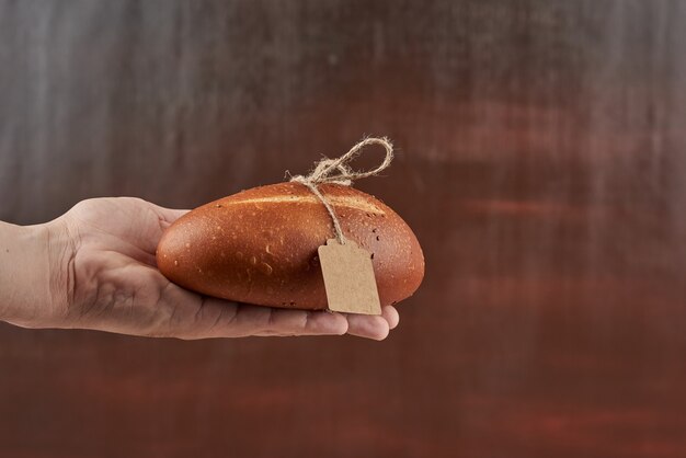 Panino di pane nella mano del fornaio con l'etichetta.