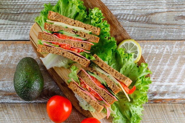 Panino di verdure con formaggio, prosciutto, limone, avocado su tagliere di legno e, piatto disteso.