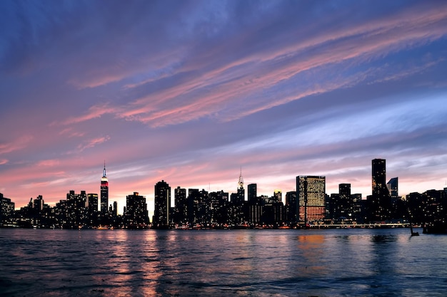 Panorama della siluetta del centro di Manhattan di New York City al tramonto con i grattacieli ed il cielo variopinto sopra l'East River