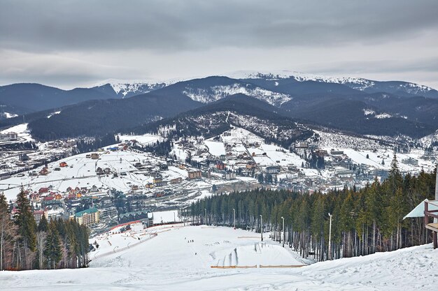 Panorama di comprensorio sciistico, piste, gente sugli impianti di risalita, sciatori in pista tra verdi pini e lance da neve. Copia spazio