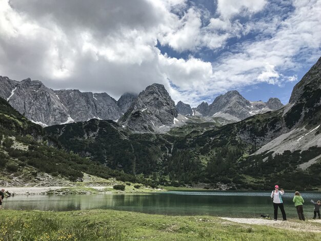 Panoramica dei turisti vicino ad un lago nella parte inferiore delle montagne circondate da alberi e piante verdi