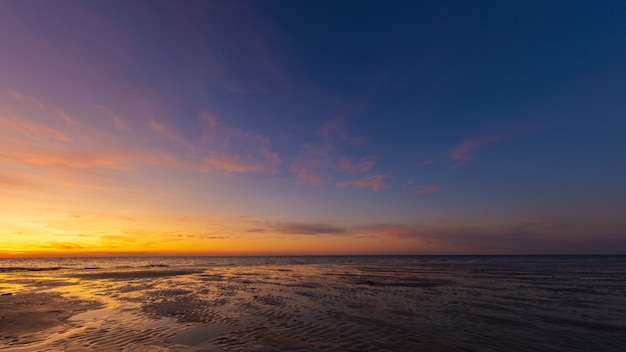Panoramica della riva bagnata della spiaggia sotto un cielo blu e giallo al tramonto