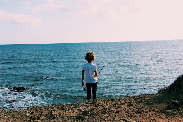 Panoramica di un bambino piccolo che sta alla spiaggia vicino all'acqua