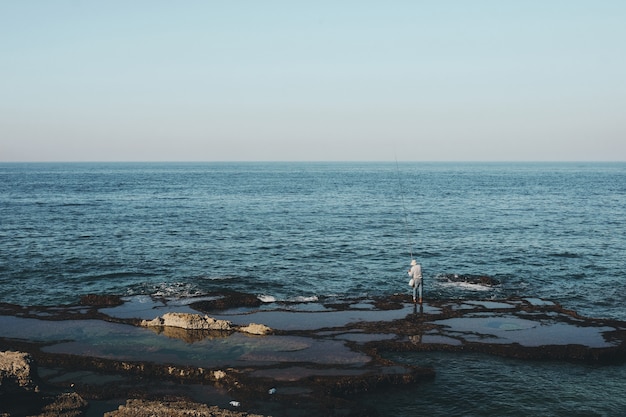 Panoramica di un pescatore che sta sulla riva durante il giorno