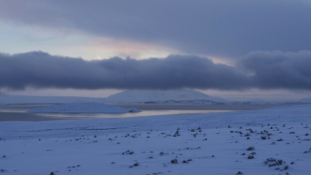 Panoramica di una riva nevosa vicino all'acqua congelata sotto un cielo nuvoloso