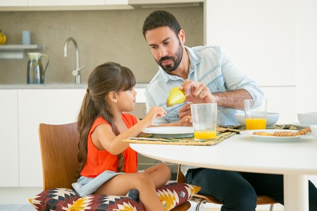 Papà bello che dà frutta alla sua ragazza mentre fanno colazione insieme in cucina