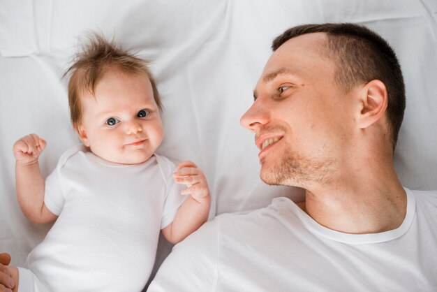 Papà bello che si trova con il bambino sveglio a letto