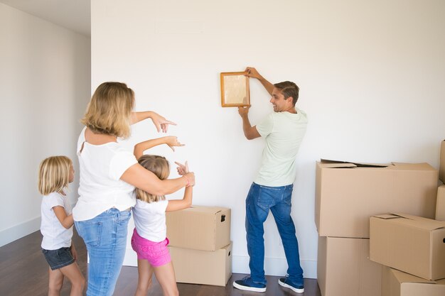 Papà caucasico in abiti casual appendere cornice vuota sul muro nella nuova casa e sorridente