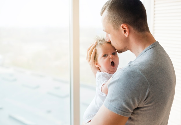 Papà che bacia bambino con la bocca aperta in fronte