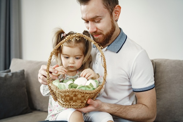 Papà con la barba. Ragazza che tiene un cestino. Padre e figlia seduti sul divano.