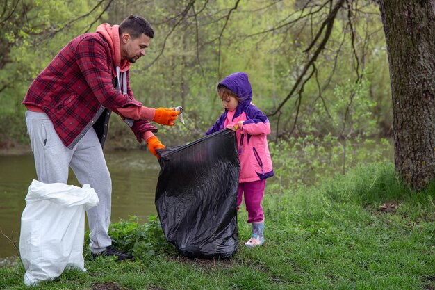Papà e figlia, con i sacchi della spazzatura, puliscono l'ambiente dalla spazzatura.