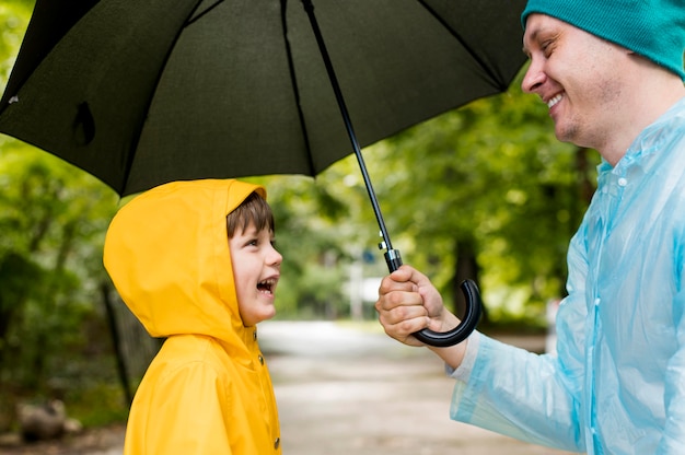 Papà e figlio sorridono l'un l'altro sotto il loro ombrello