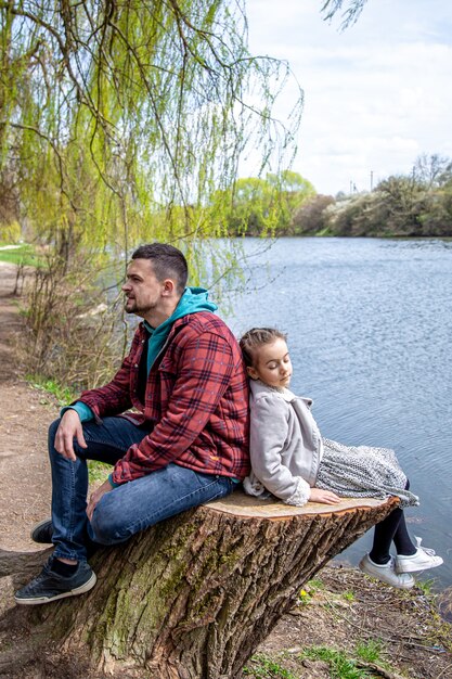 Papà e sua figlia si siedono nella foresta vicino al fiume all'inizio della primavera e si godono la natura.