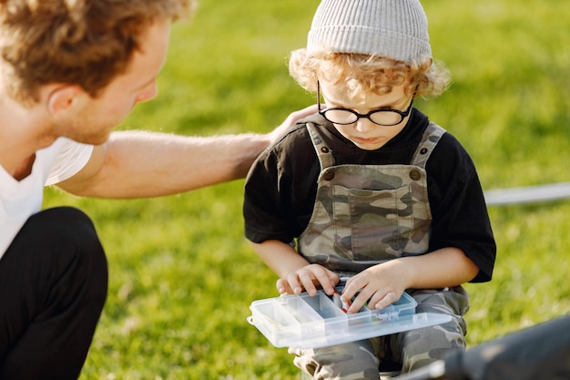 Papà e suo figlio trascorrono del tempo insieme all'aperto. Ragazzo riccio del bambino che indossa un camice color cachi. Ragazzo seduto su un secchio e ascolta suo padre