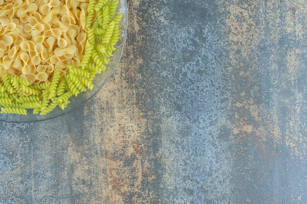 Papillon e fusilli nella ciotola, sul piano di marmo.