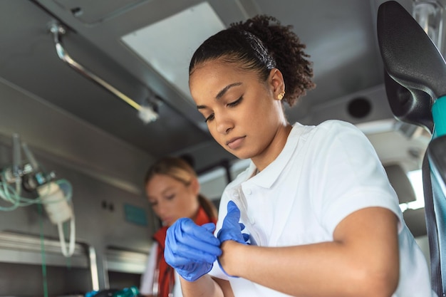 Paramedico femminile afroamericano che si toglie i guanti Due paramedici che aiutano il paziente ferito