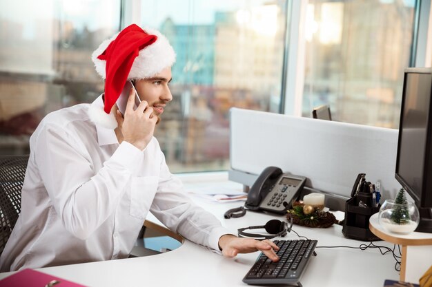 Parlare sorridente dell'uomo d'affari sul telefono al giorno di Natale di worplace.