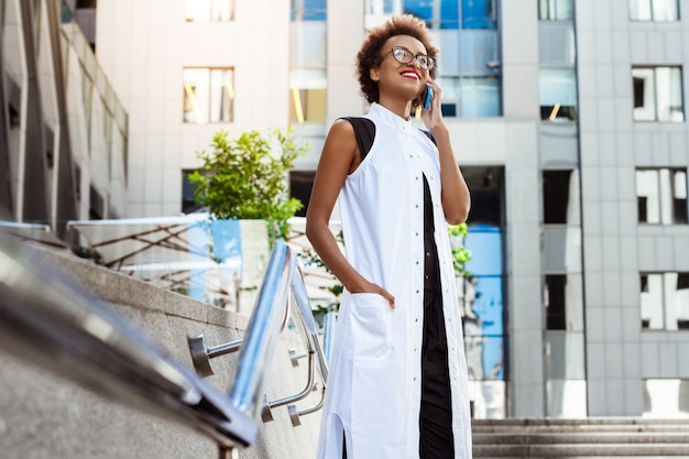 Parlare sorridente della bella donna sul telefono che cammina giù la città